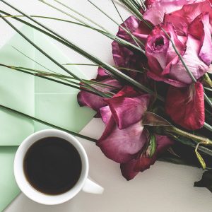 a bouquet of flowers, a cup of coffee, and a mint green envelope